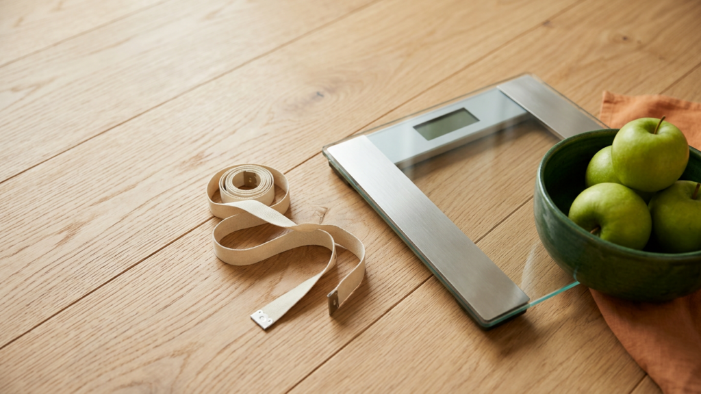 Measuring tape, bathroom scale and green apples on a wooden floor for a BMI and waist-to-height ratio calculator